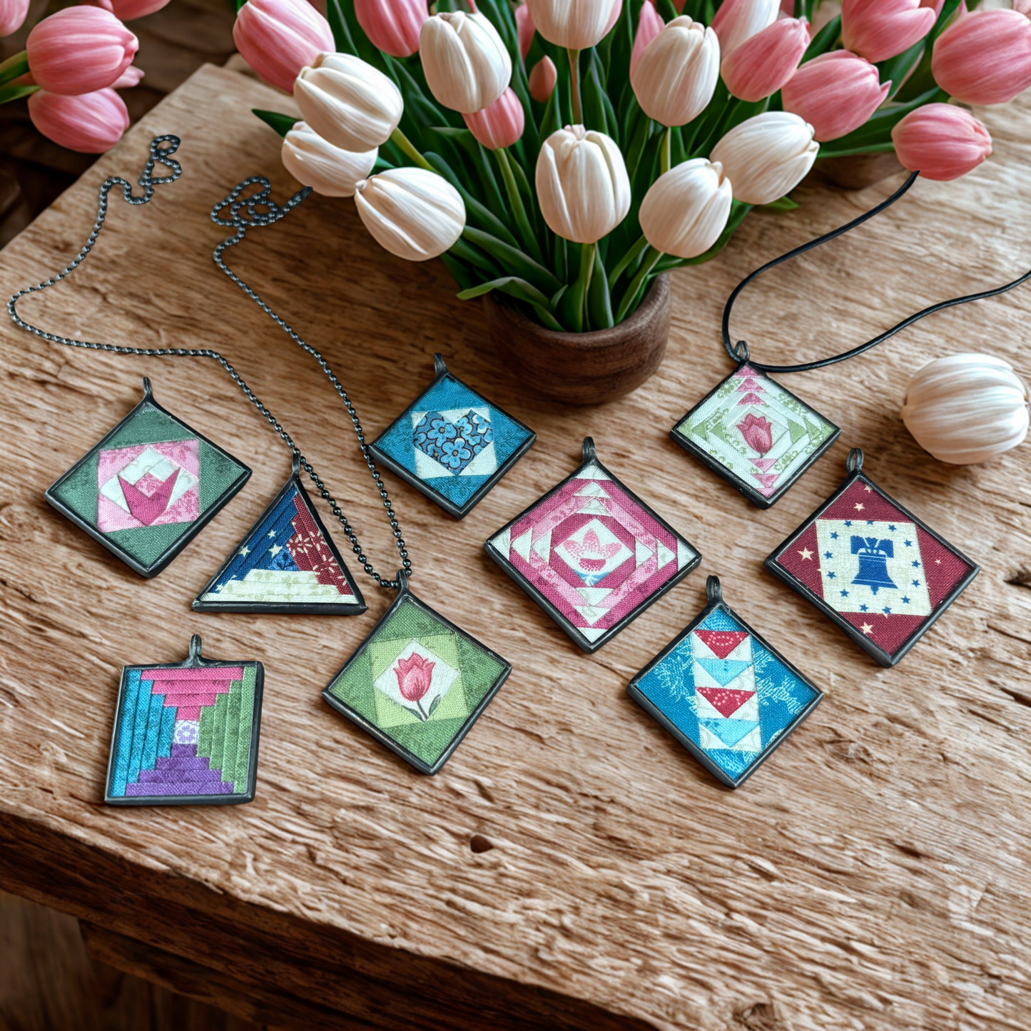 Colorful geometric pendants on necklaces with tulips in the background on a wooden surface