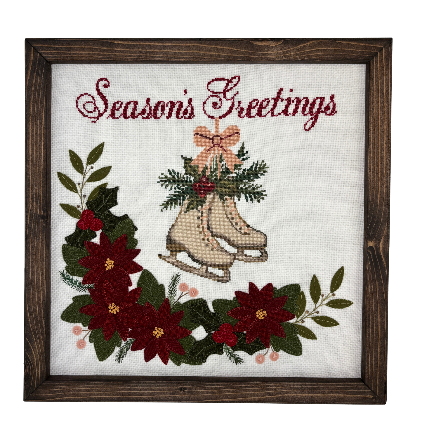Framed cross-stitched and wool applique with 'Season's Greetings' text, ice skates, and poinsettias.