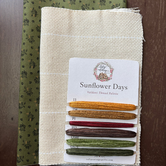 A fabric and thread palette set called 'Sunflower Days', featuring a beige card with six thread samples in yellow, gold, red, brown, sage green, and olive green, layered over a patterned olive green fabric, all displayed on a dark wood background.