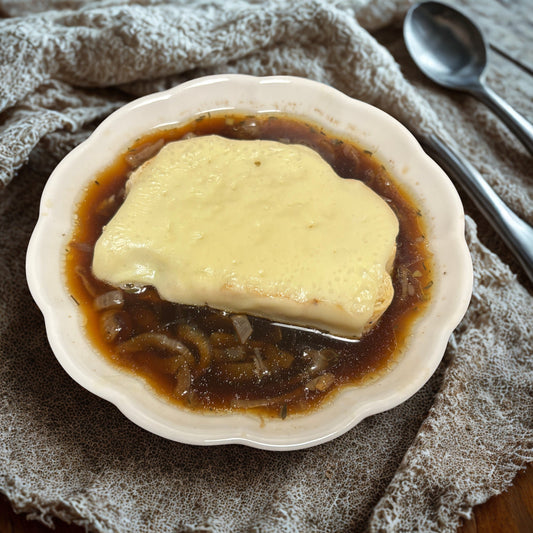 Bowl of soup with a slice of bread in it, sitting on a table with a spoon.