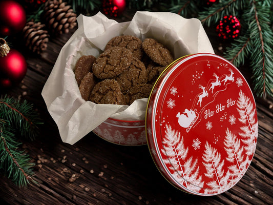 red Christmas tin filled with cookies on a wooden surface with pine branches and christmas decorations in the background.