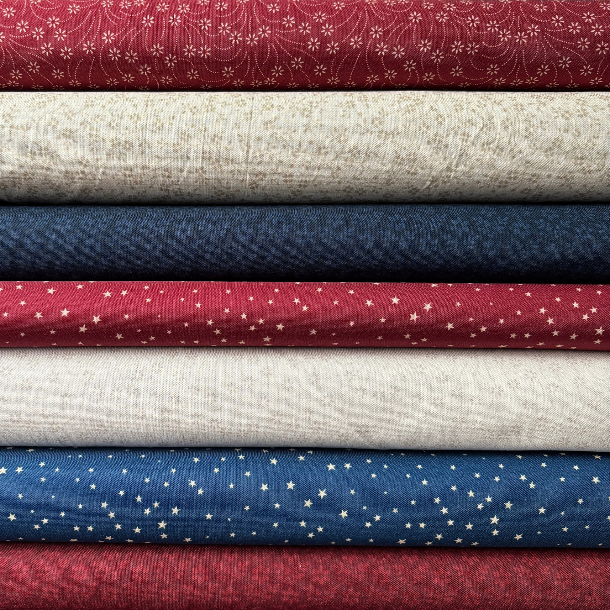 Stack of fabric swatches in red, white, blue, and beige with various patterns.