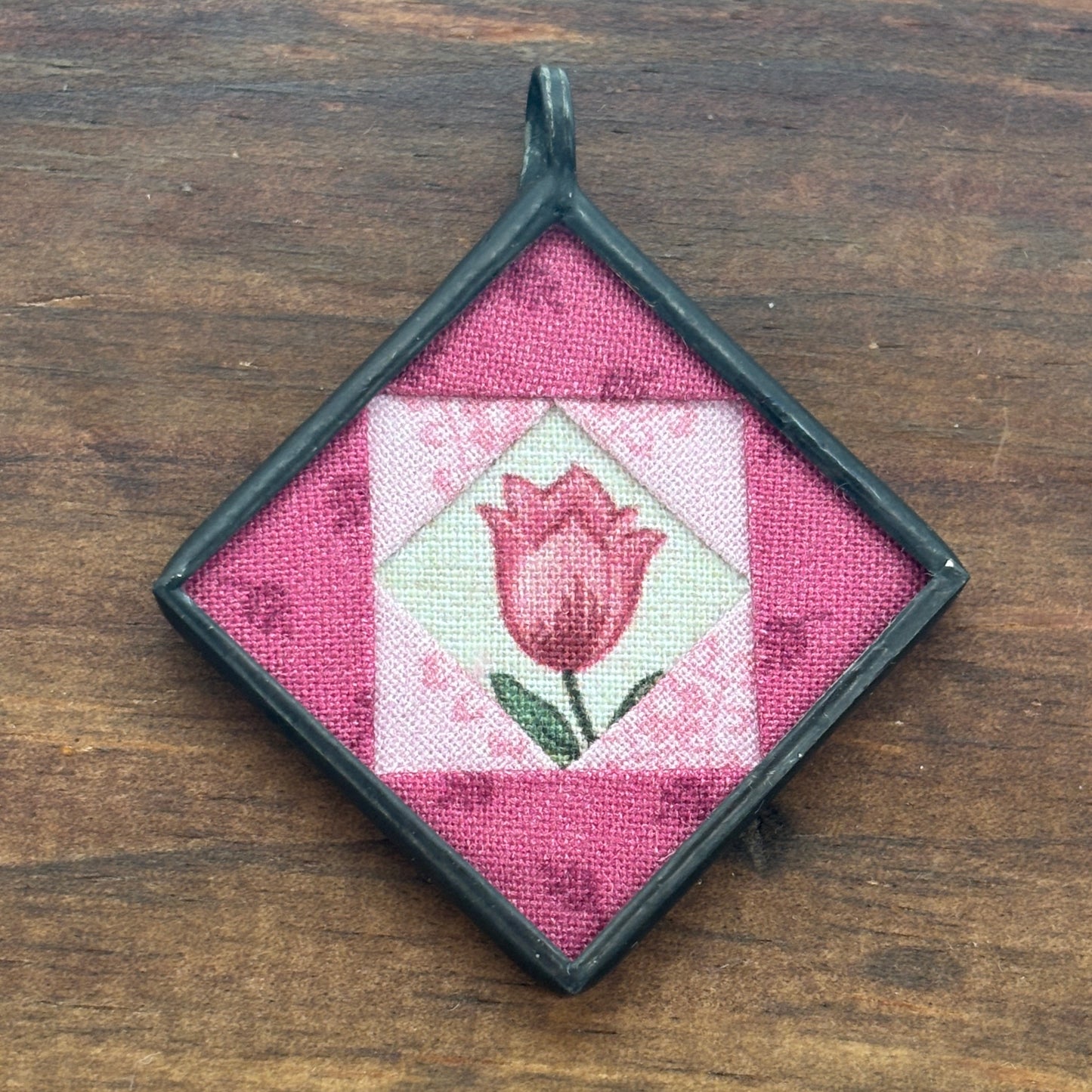 Square pendant with pink tulip design on a wooden surface
