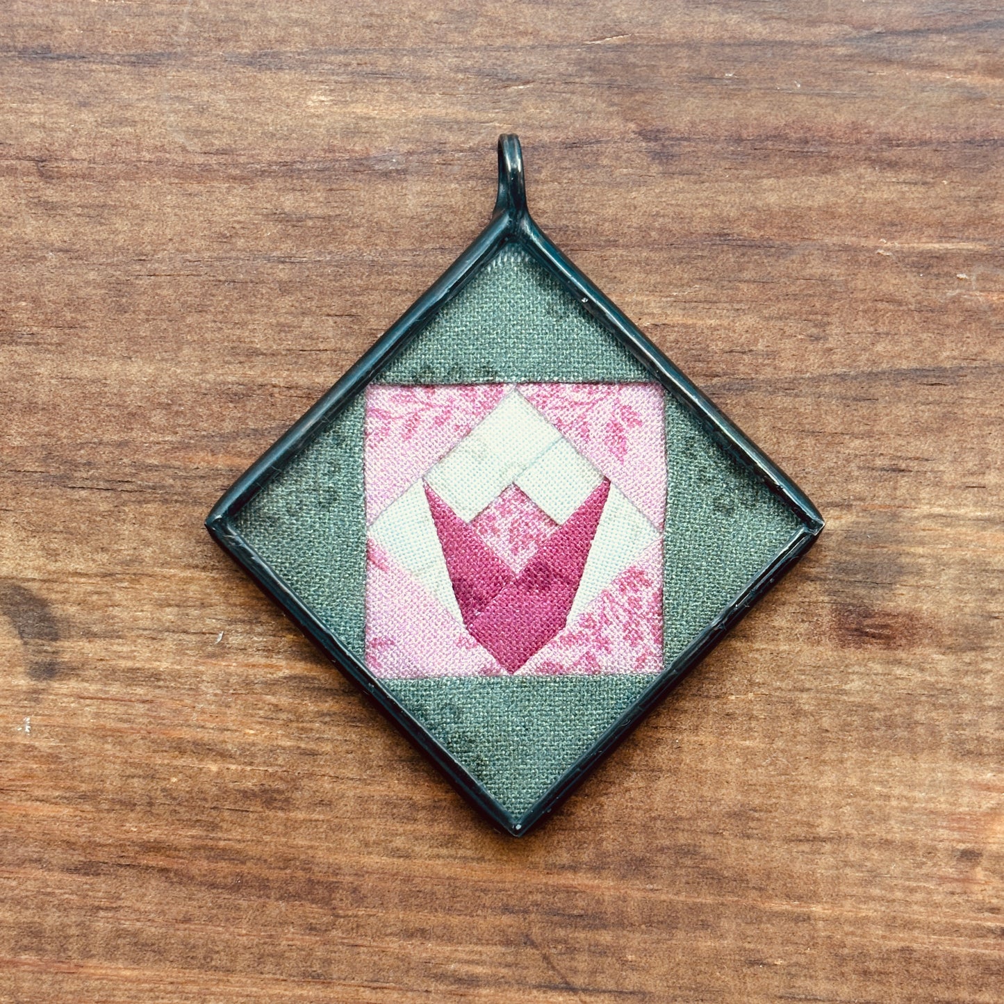 Square green pendant with pink and white tulip design on a wooden surface
