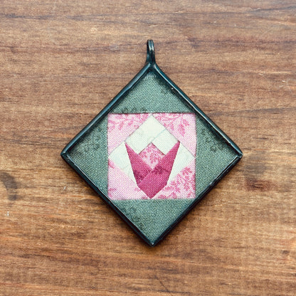 Square green pendant with pink and white tulip design on a wooden surface