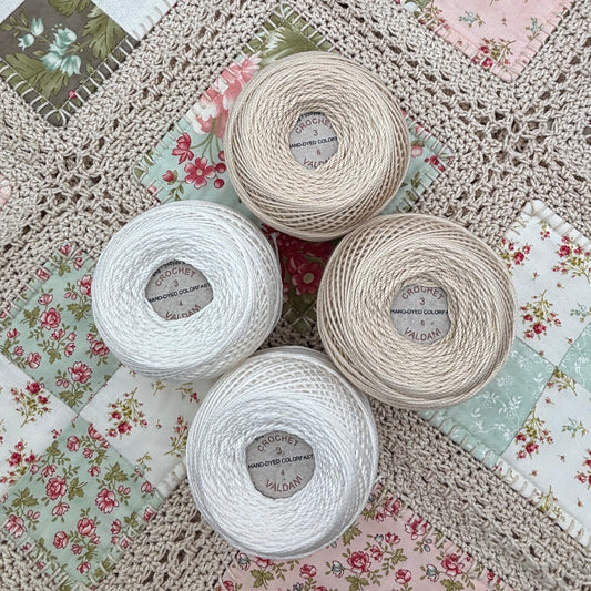Four skeins of Crochet Cotton on a textured fabric background