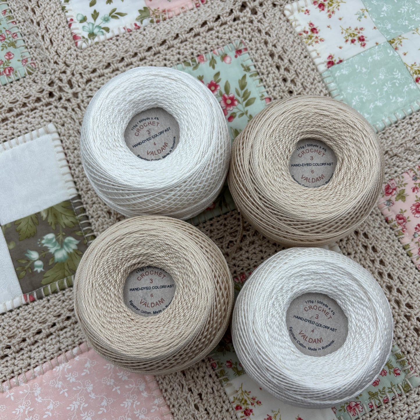 Four spools of yarn on a crocheted surface with a patchwork background