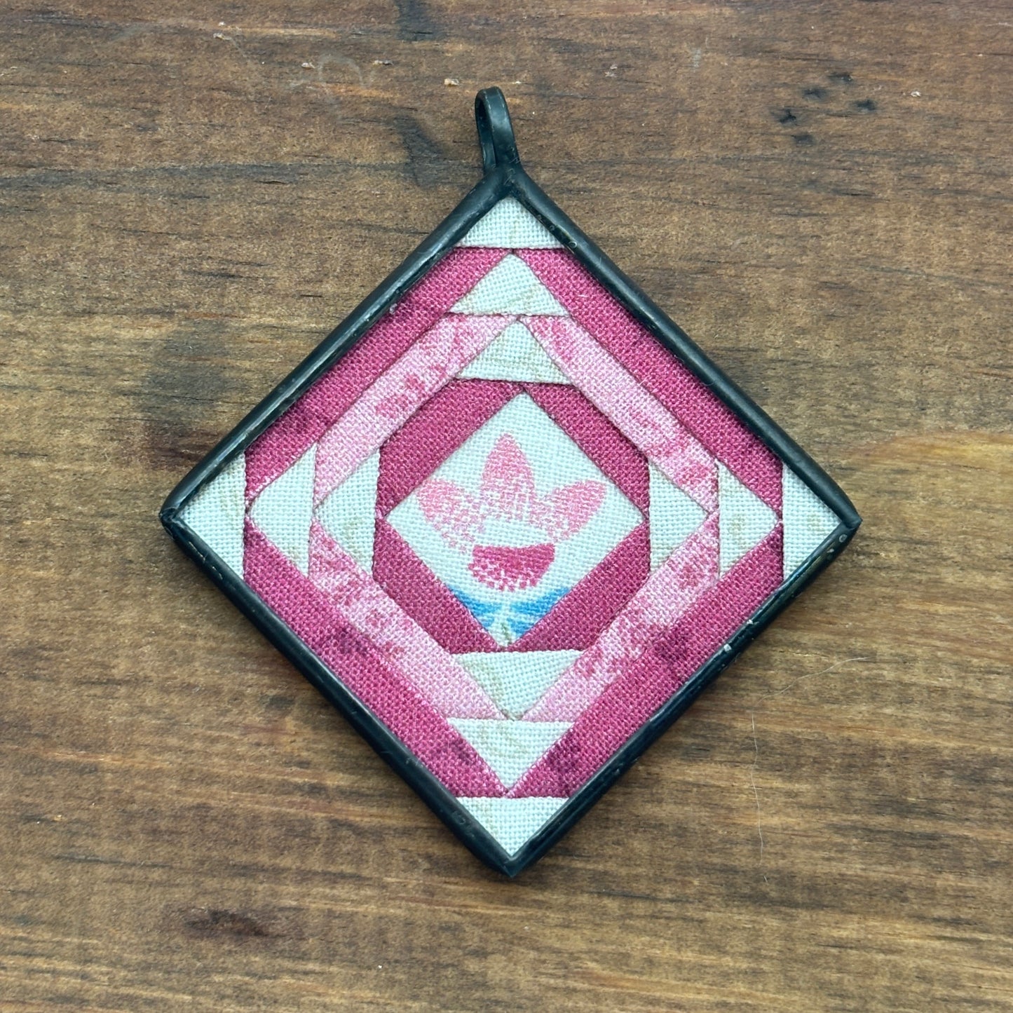 Quilted square pendant with geometric pattern on a wooden surface