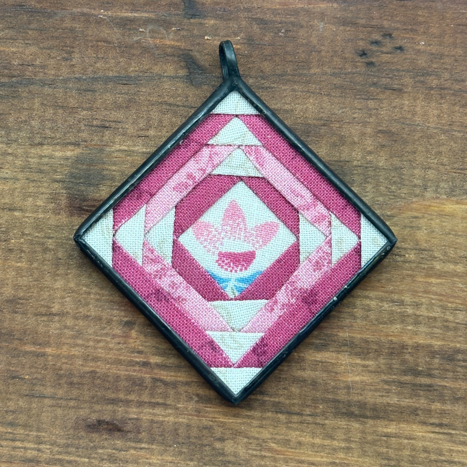 Quilted square pendant with geometric pattern on a wooden surface