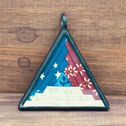 Triangular pendant with a log cabin design in patriotic colors on a wooden background