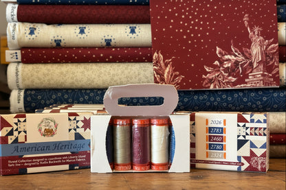 Collection of fabric bolts and thread spools on a cutting mat with 'American Heritage' branding.