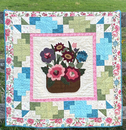Quilt with floral design and flower pot hanging on a wooden fence