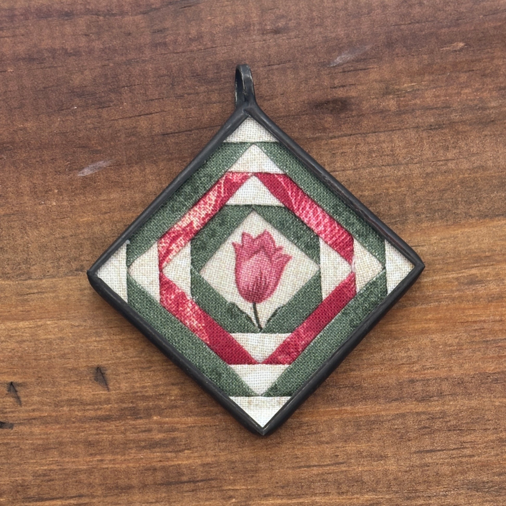 Decorative pendant with geometric pattern and central tulip design on a wooden surface