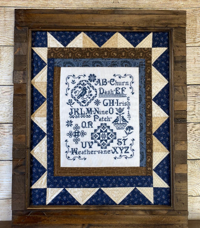 Framed cross-stitched sampler with quilted border in a wooden frame.