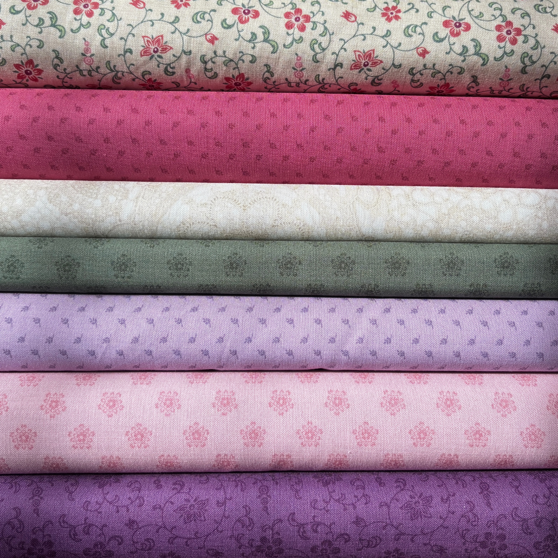 Stack of fabric bolts with floral and patterned designs in various colors.