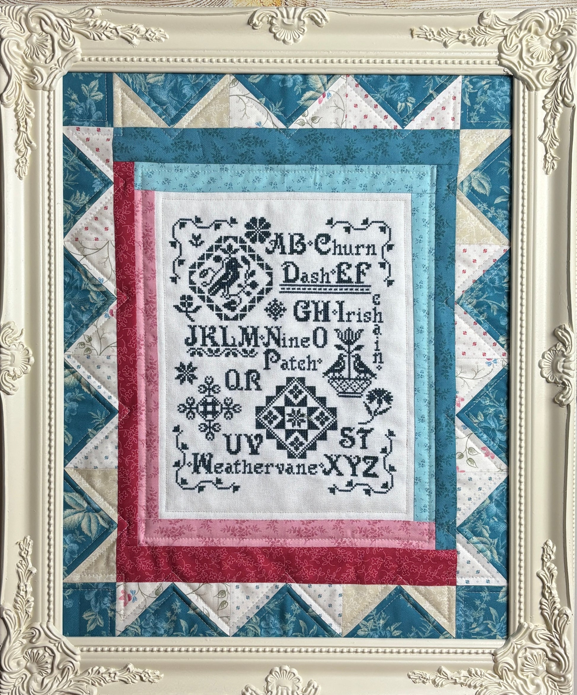Quilt with cross-stitched text and decorative border in a decorative frame.