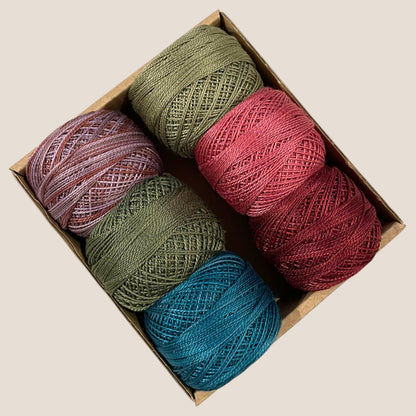 Box of perle cotton balls in various colors on a beige background