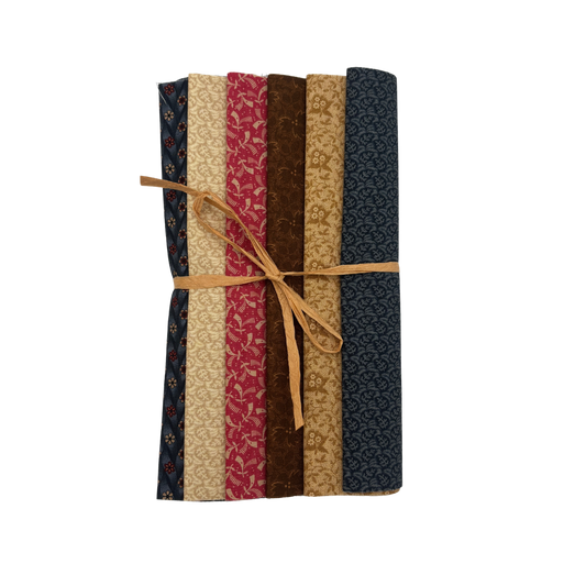 A bundle of six patterned quilting fabrics tied together with a tan string, displayed vertically against a plain white background.