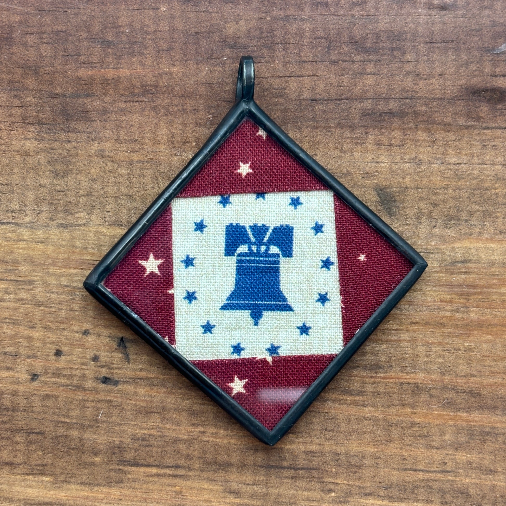 Pendant with Liberty Bell design on a wooden surface