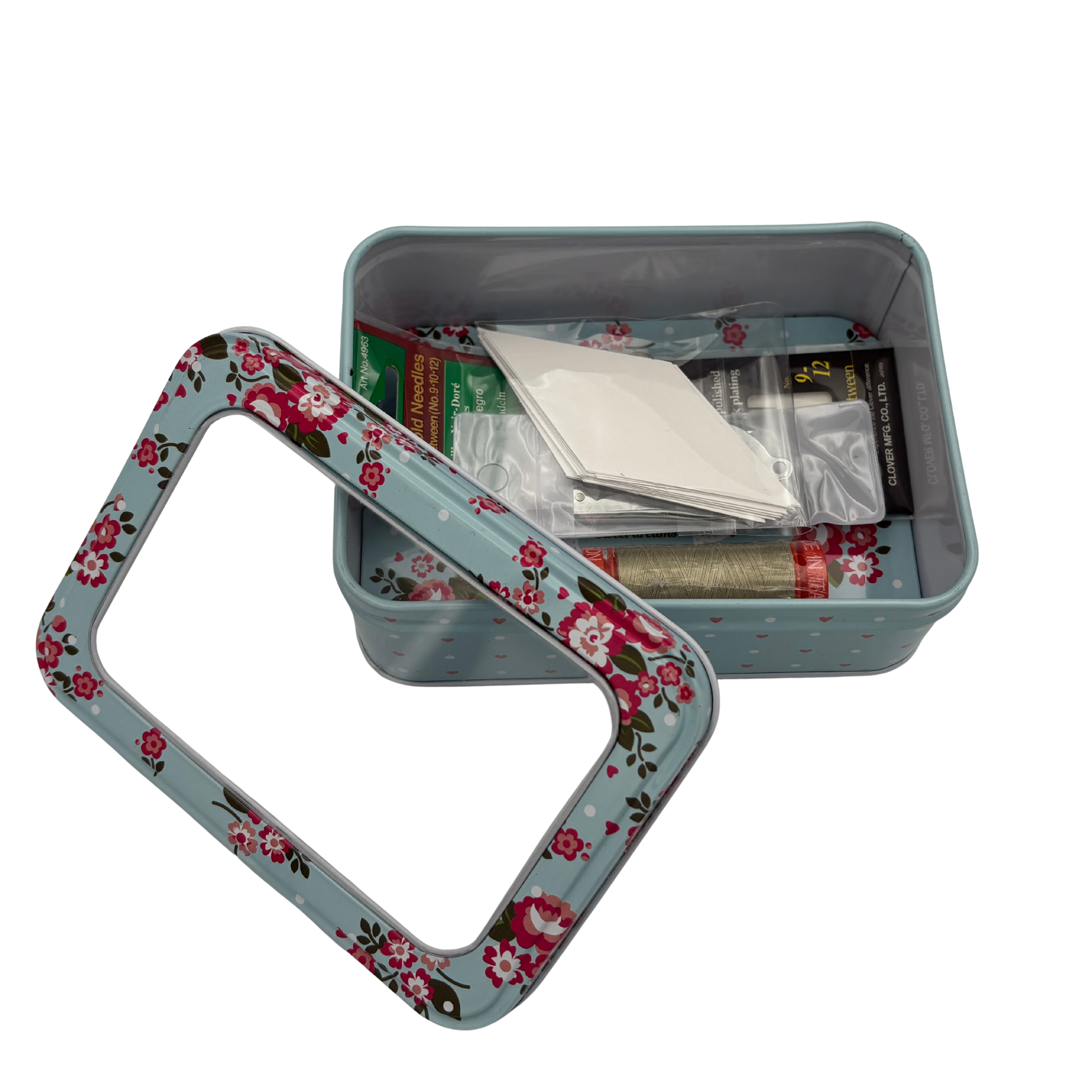 Floral-patterned metal tin with stitching items inside and a lid on a white background