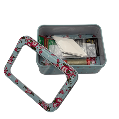 Floral-patterned metal tin with stitching items inside and a lid on a white background