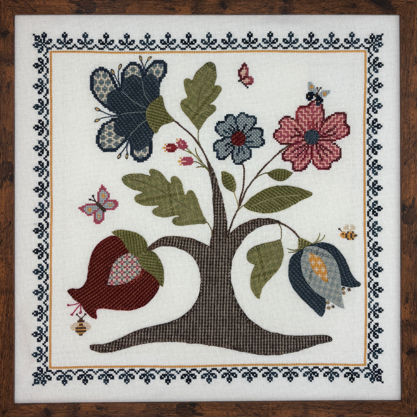cross stitch and wool applique design of a tree with flowers, butterflies, and bees on a white background.