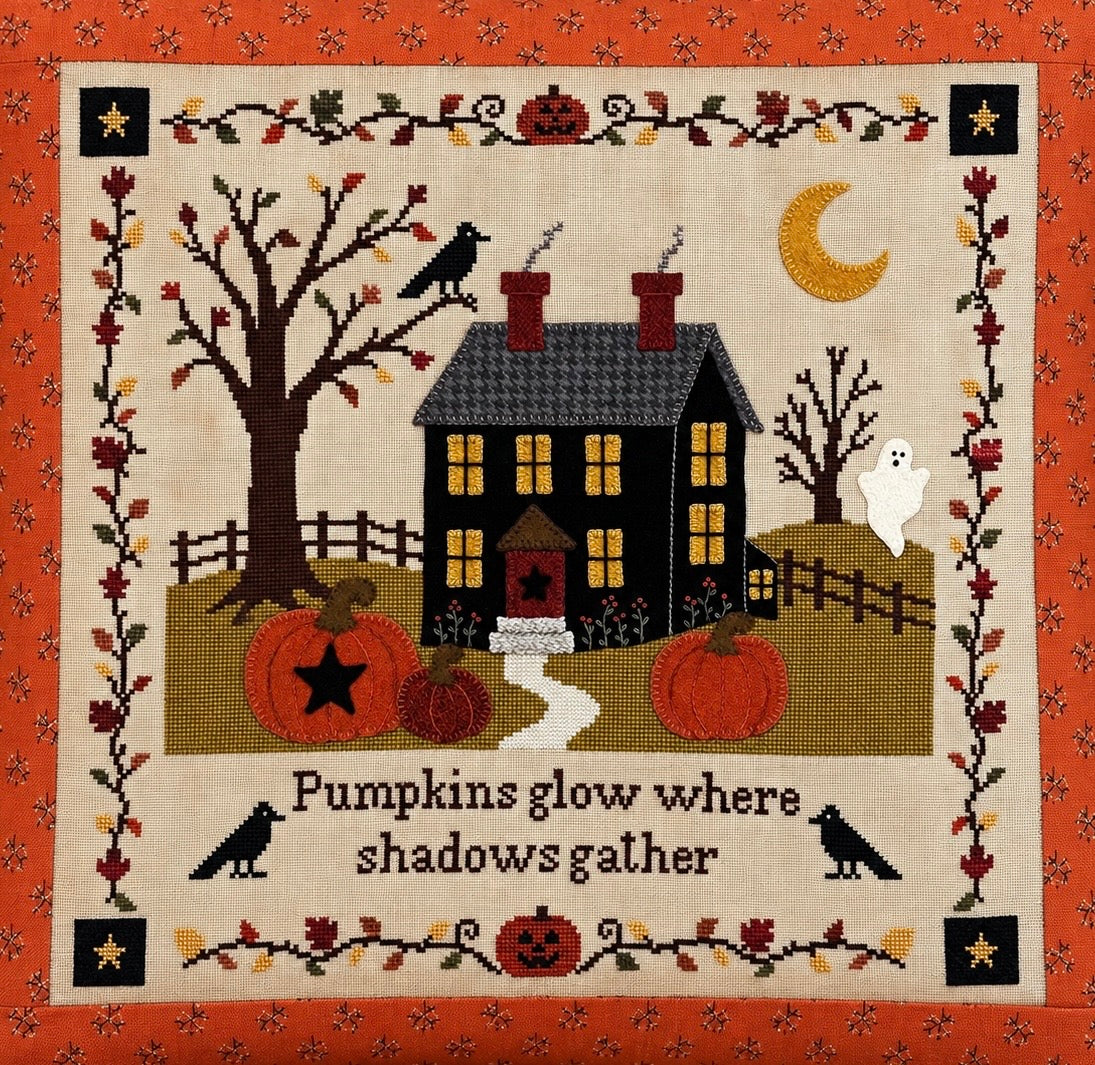 A square cross-stitch and wool applique pillow featuring a haunted house, pumpkins, bare trees, crows, a ghost, a crescent moon, and the phrase 'Pumpkins glow where shadows gather' on a cream background with an orange patterned fabric border.