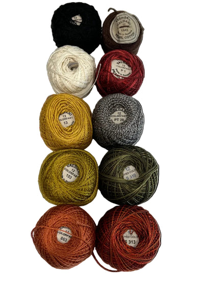 Nine skeins of yarn arranged in a vertical column on a white background, showing a variety of colors including black, cream, brown, red, mustard yellow, gray, olive green, terracotta orange, and rust red.