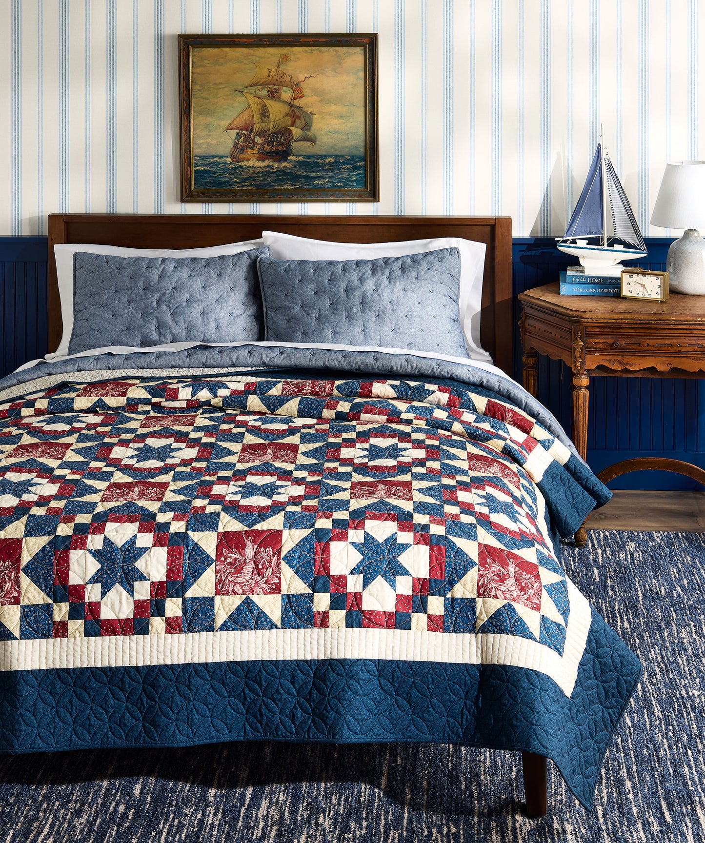 Bedroom with a quilted bedspread featuring a geometric pattern, blue walls, and a ship painting on the wall.