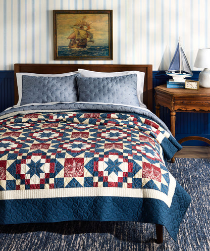 Bedroom with a quilted bedspread featuring a geometric pattern, blue walls, and a ship painting on the wall.