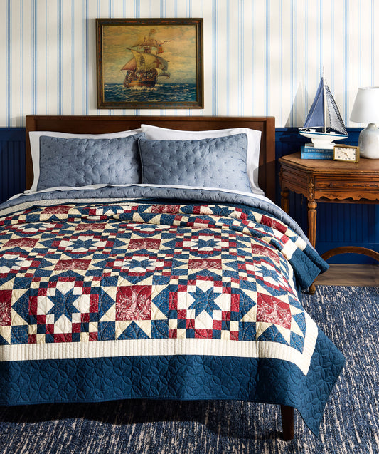 Bedroom with a quilted bedspread featuring a geometric pattern, blue walls, and a ship painting on the wall.