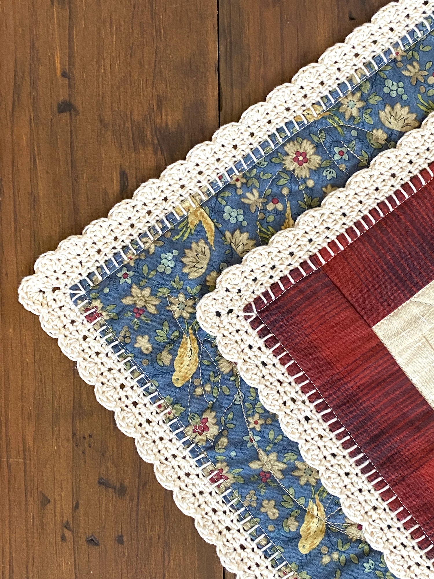 Close-up of a patchwork table runner with floral patterns and crochet trim on a wooden surface.