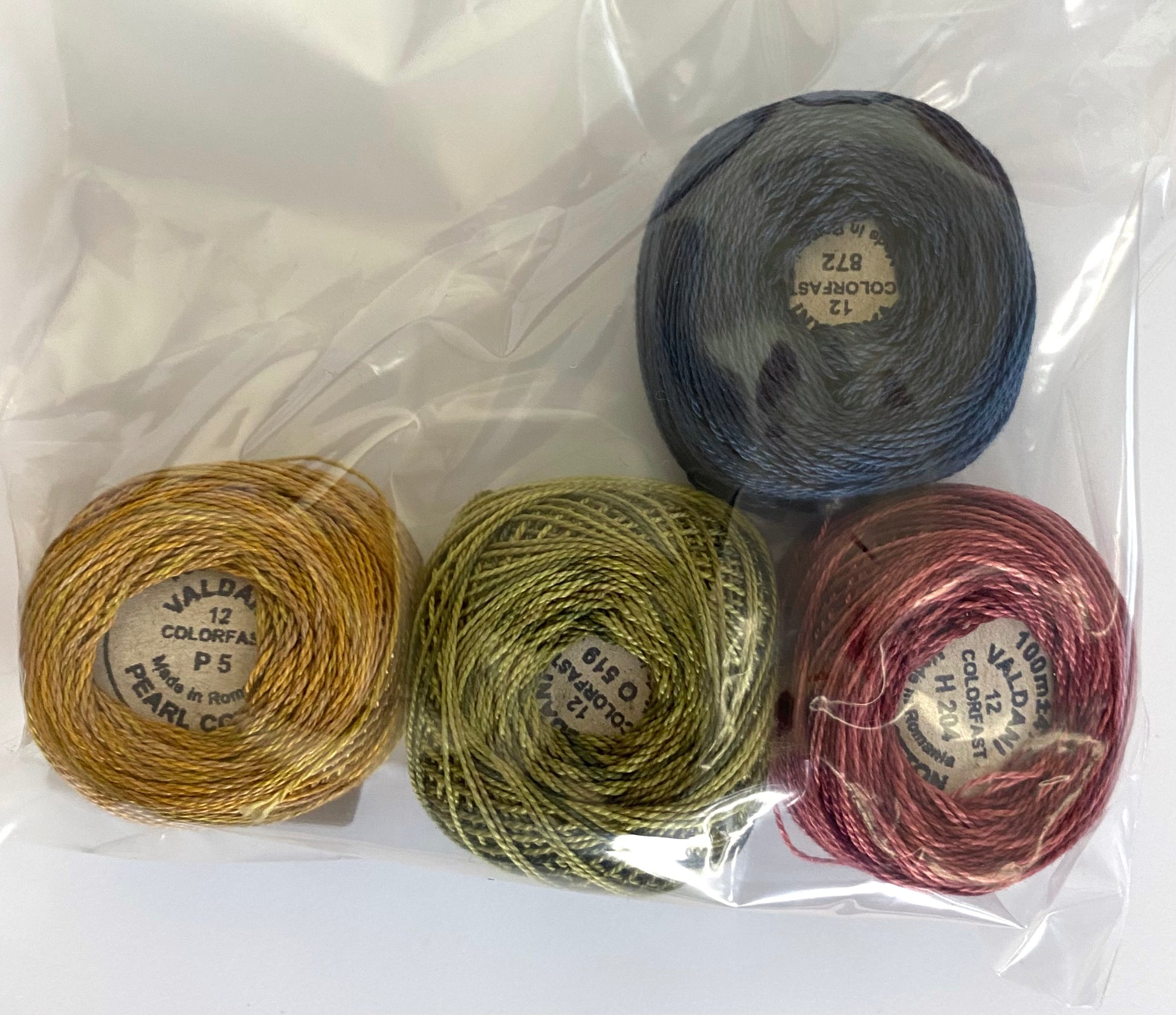 Four skeins of yarn in gold, green, blue, and pink on a white background