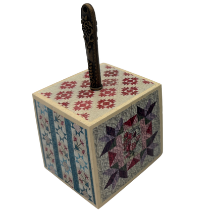 Wooden block with quilt patterns and a seam ripper on a white background