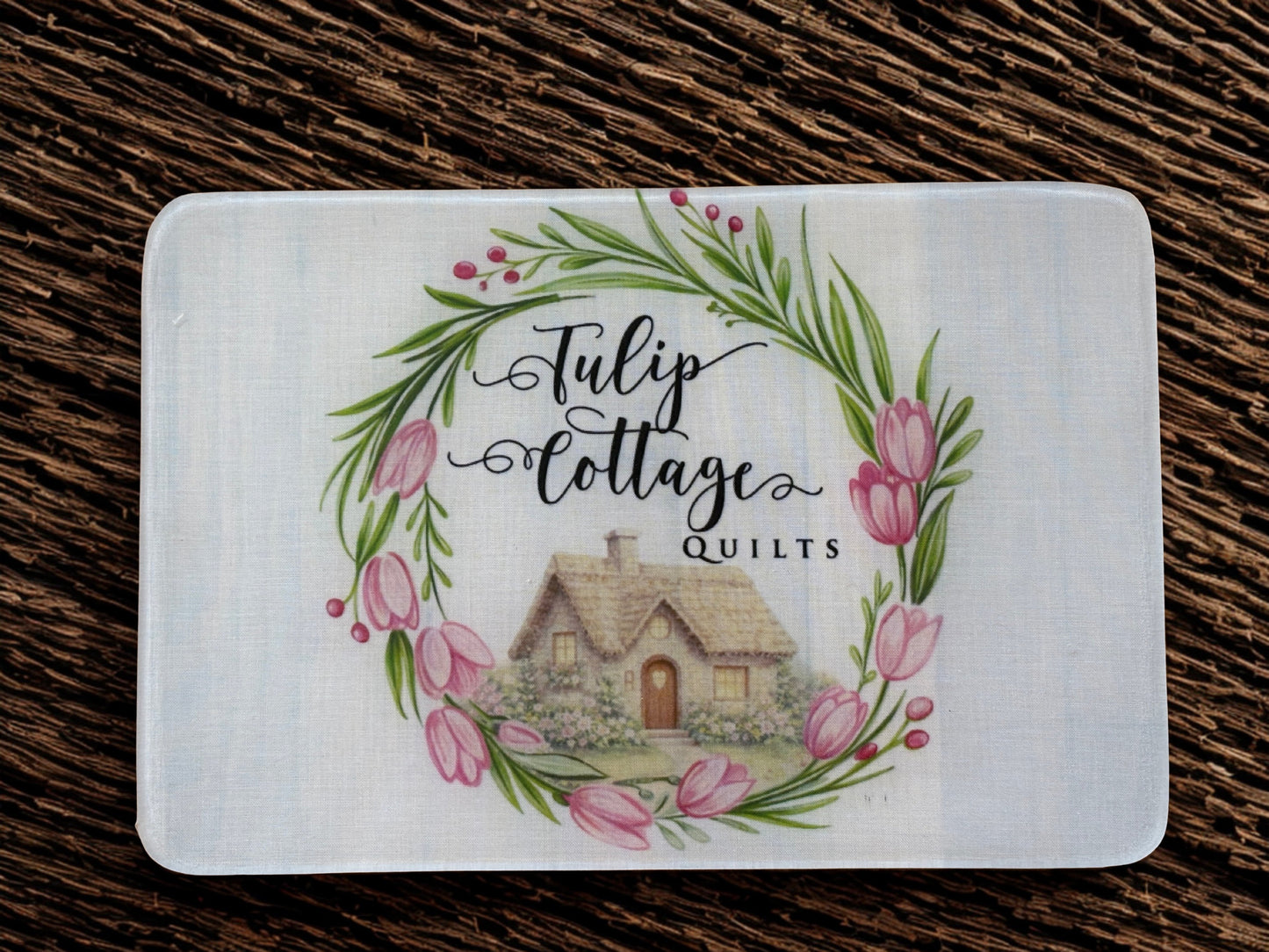 Card with 'Tulip Cottage Quilts' design featuring a cottage and floral wreath on a wooden surface.